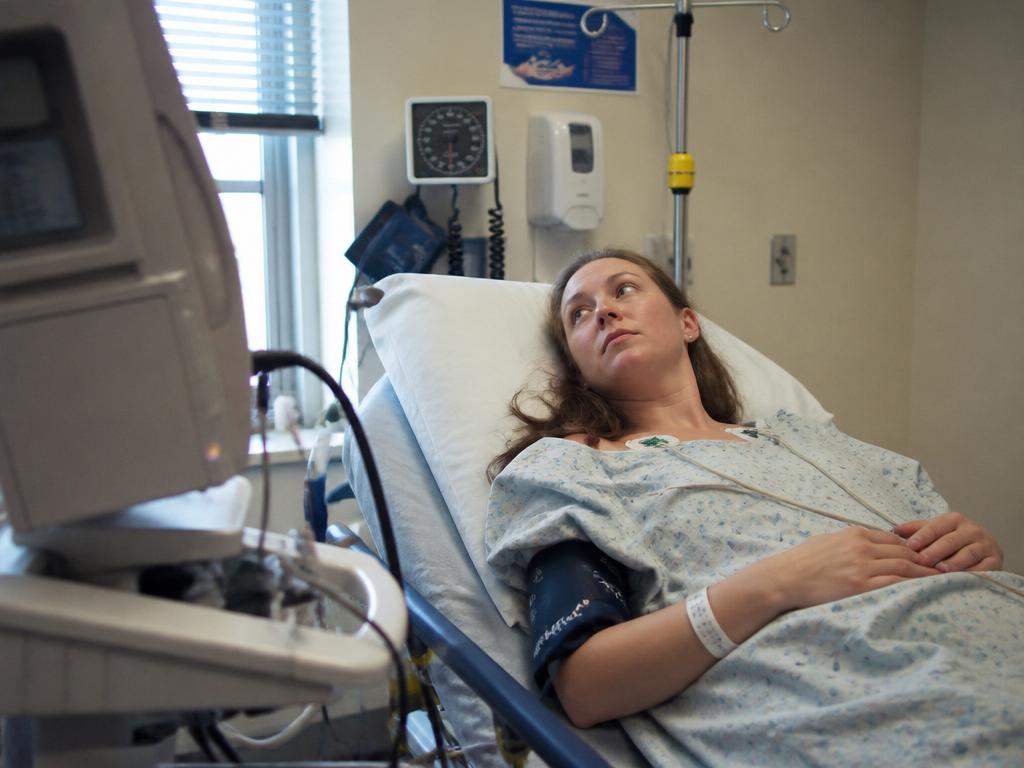 A woman lies on a partially tilted medical exam table with a blood-pressure cuff and ECG electrodes, waiting calmly during a test.